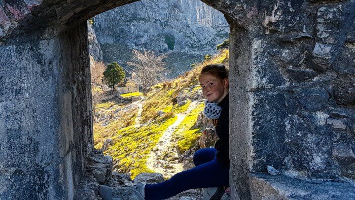 Traveling with teenagers to amazing places like Kotor. A teen sitting in a stone window frame with a stone church in the background on their best vacations for families with teenagers.