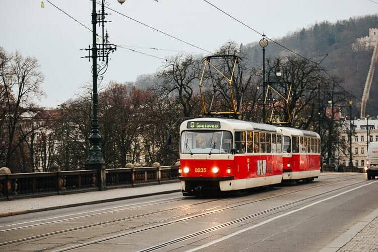 a classic red and white Prague tram crossing bridge. The trees around the bridge have lost their leaves and it looks like a dull day in Prague