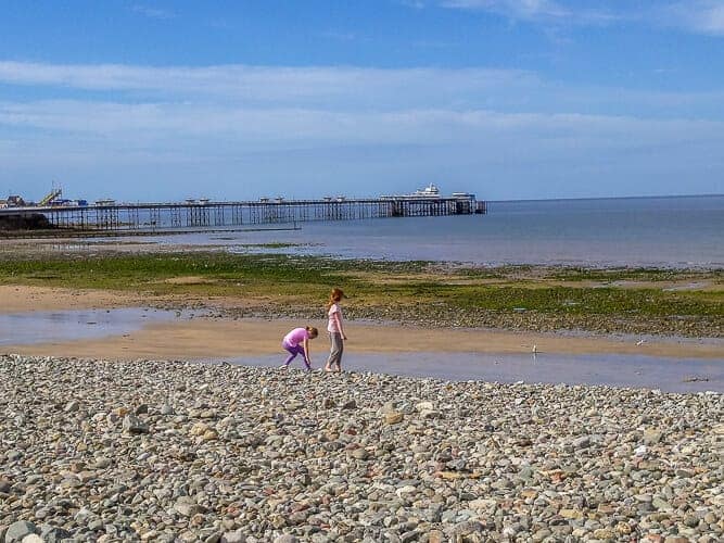 The girls of Wyld Family Travel playing on the Llandudno beach. The tide is out exposing some rocks and seaweed with the Llandudno pier in the background