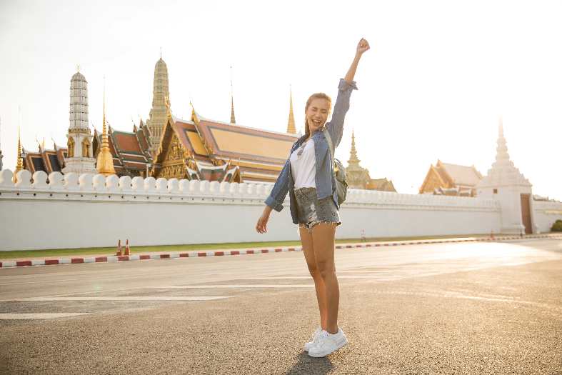 a teenage girl posing for a photo outside the walls of the grand palace in bangkok
