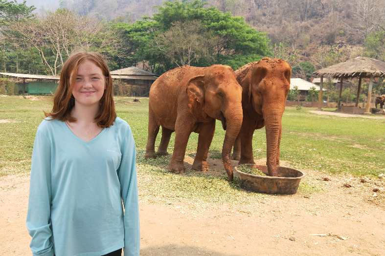 a teenage girl posing for a photo in front of two elephants at an elephant sanctuary in Thailand