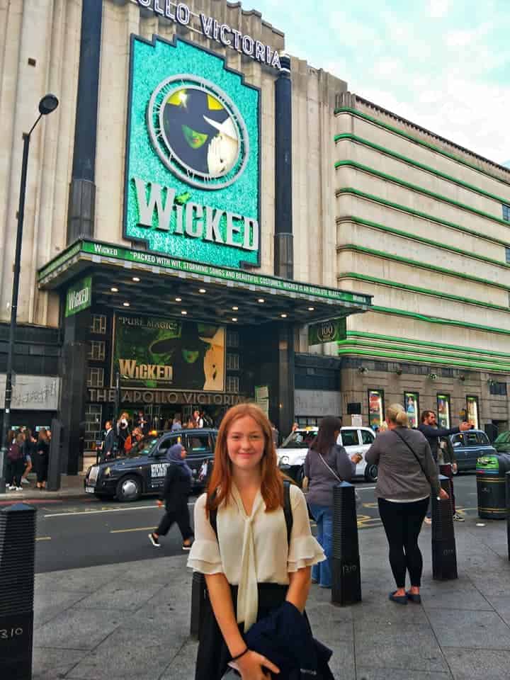 Willow standing out the front of the theatre showing Wicked. There is the big poster advertising it and lights showing it is ready to go.