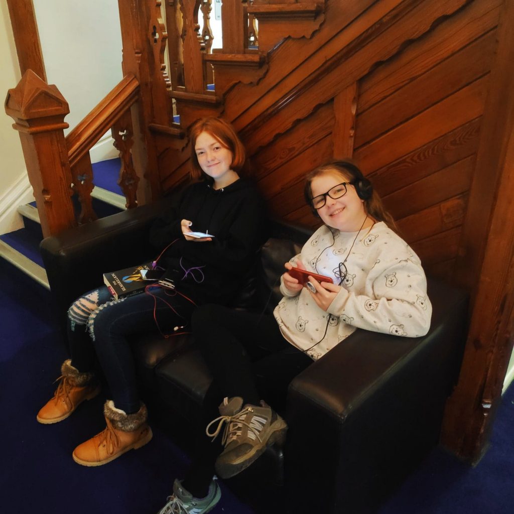 2 kids relaxing at the YHA Canterbury in the lobby listening to music and using their phones