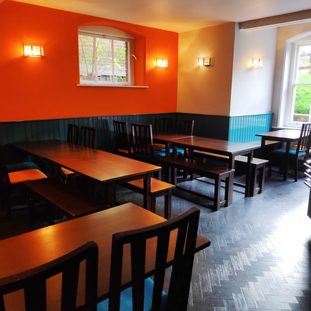 Dining room at Canterbury YHA with plenty of dark wood tables and chairs for people to sit on. SOme are picnic tables and some are full dining tables with chairs