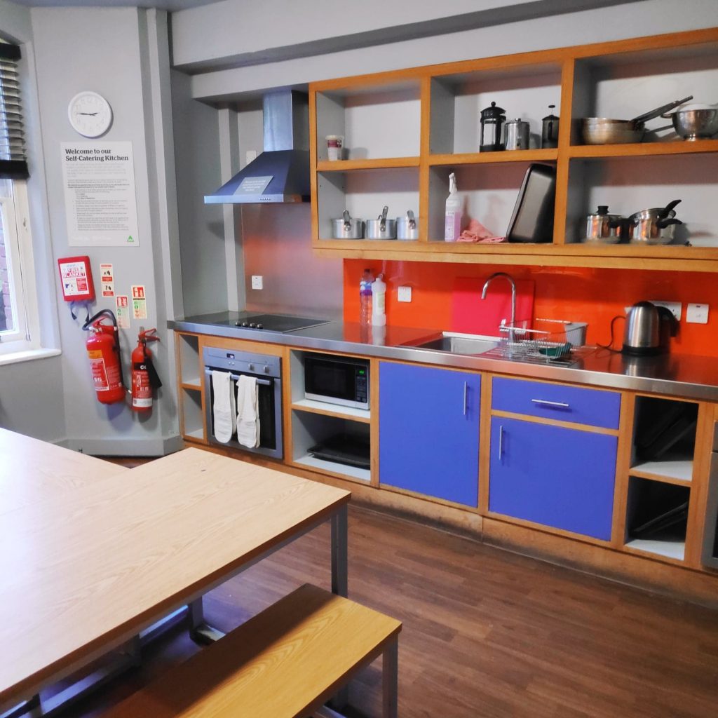 The colourful Kitchen at YHA Canterbury with blue cupboards and orange splash backs it looks fully stocked for a big cook up.