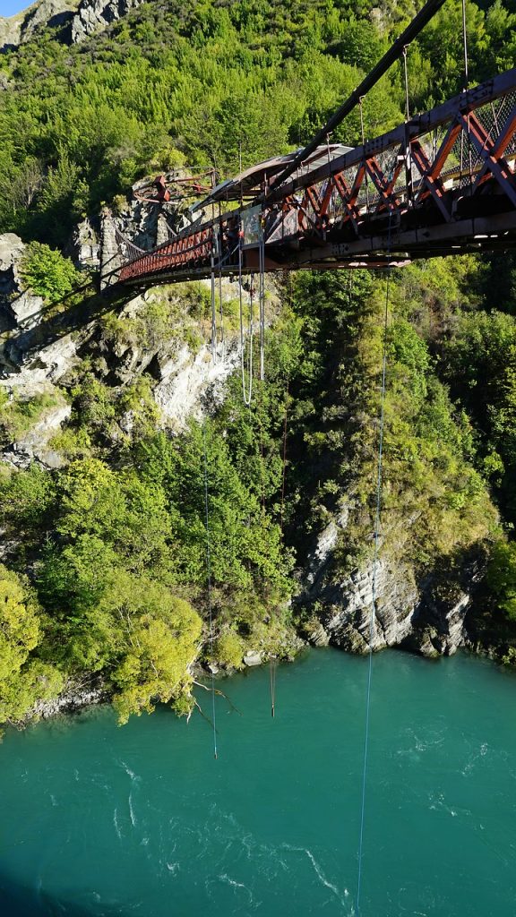 a bridge in New Zealand with people doing bungy jumping from it. Bungy jumping is one of the most adventurous things to do in Queenstown with teenagers