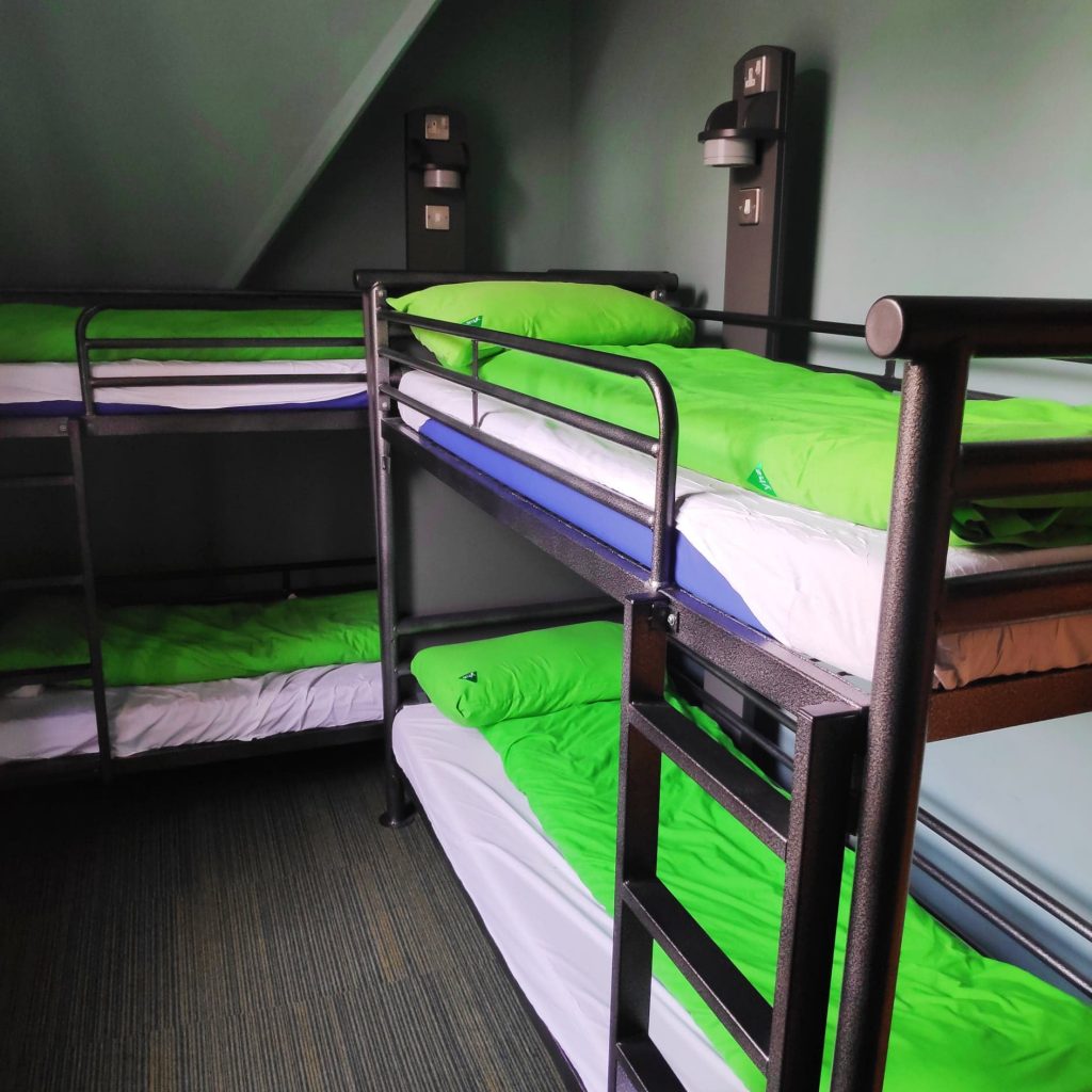 Dorm room at YHA Canterbury with 2 sets of bunk beds and green doona covers