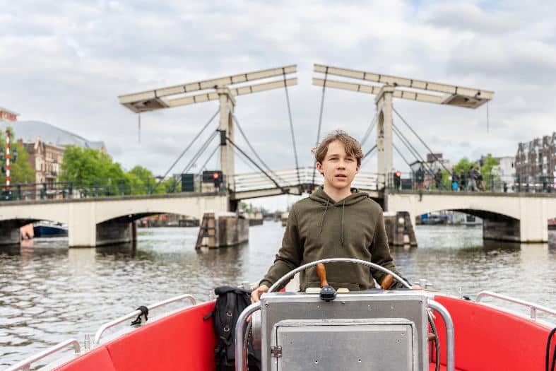 a teenage boiy having a tirn at steering a boat in the canals of Amsterdam