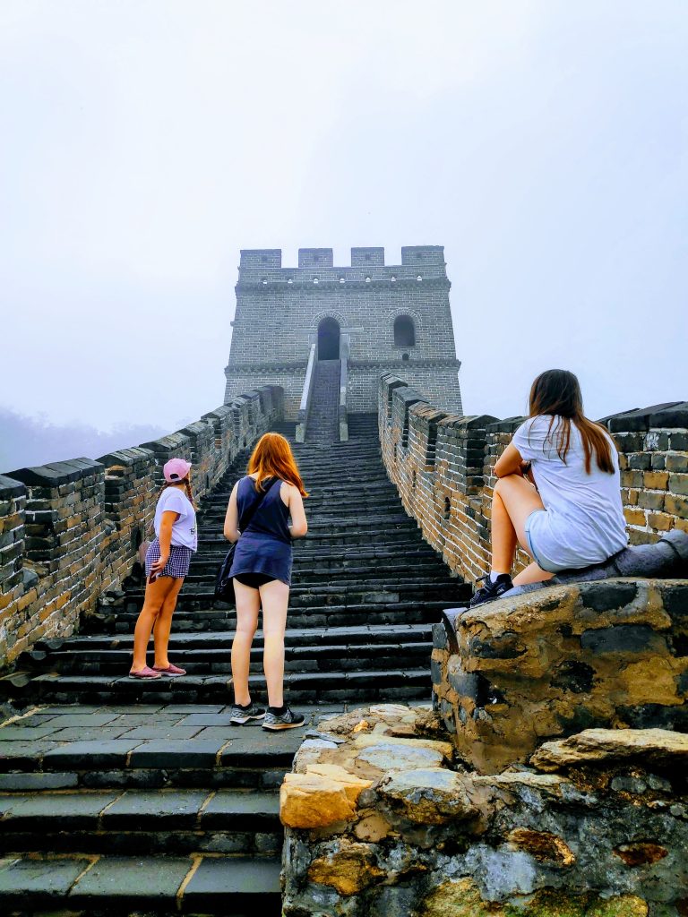 Keeping teens social while travelling can be hard for them and their parents. Here there are 3 teens girls standing on the Great Wall of China on a cloudy day