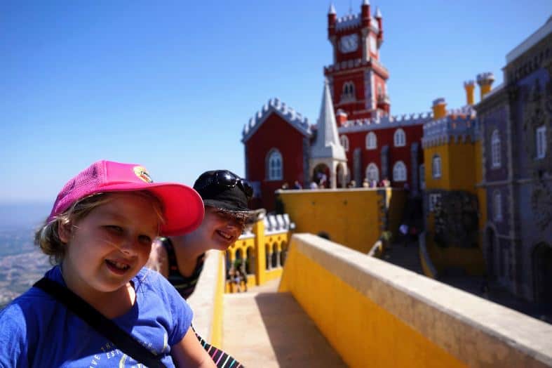 two young girls sitting on a wall posing for pictures at sintra