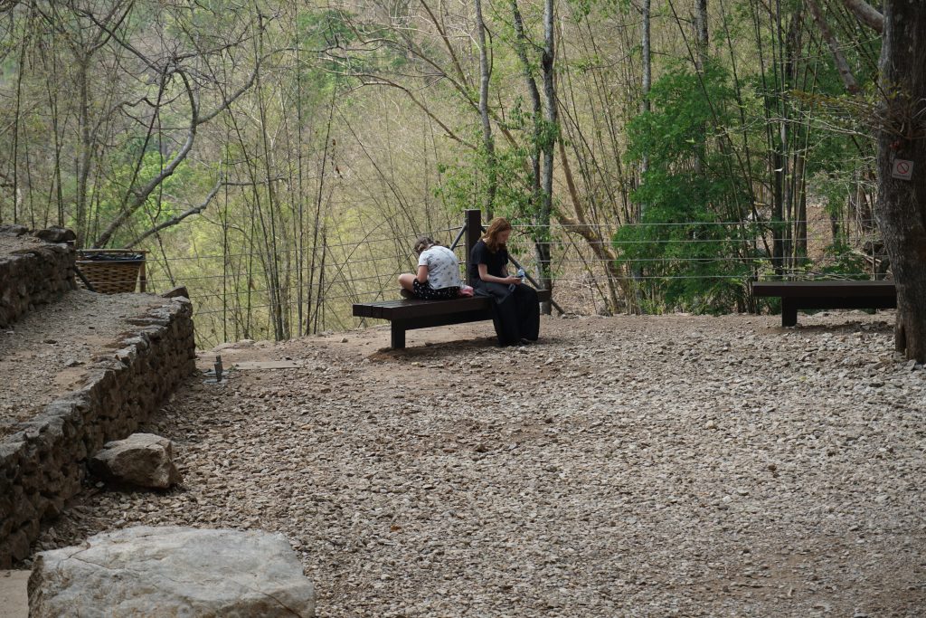 Two kids sitting on a wooden bench at Hell fire Pass. Both seem to be lost in their thoughts and ;looking very sombre