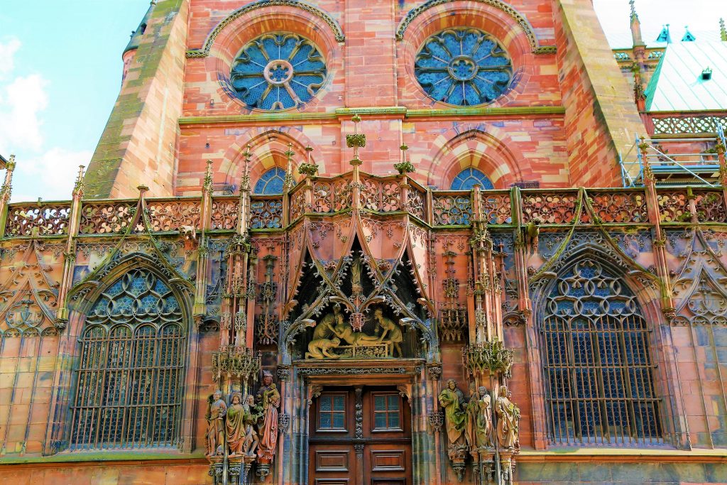 The out side of the Strasbourg Cathedral. The red brick with the sandstone arches and stained glass windows rise up to the top of the picture