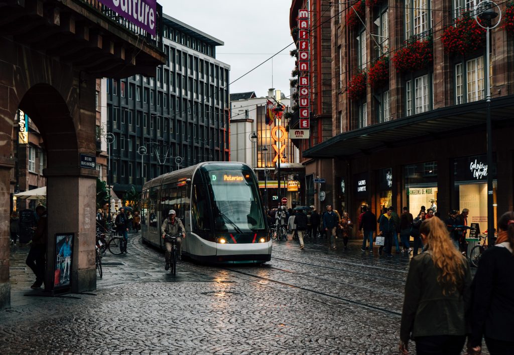 A train coming through the wet streets of Strasbourg near on dark. The street lights and the shop lights are reflecting off the wet pavement