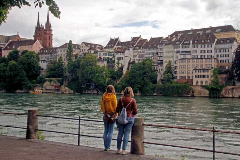 two young adults standing by the river in basel looking at the sites