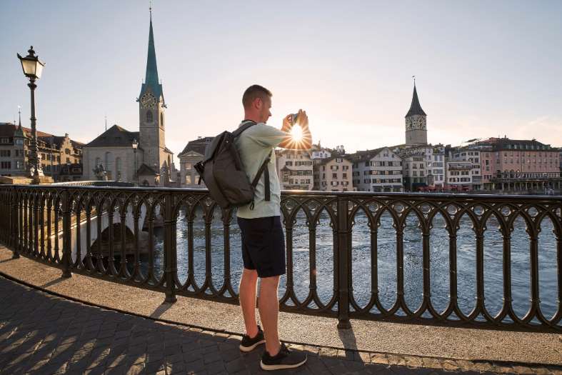 A young adult male standing by the river in Zurich taking pictures