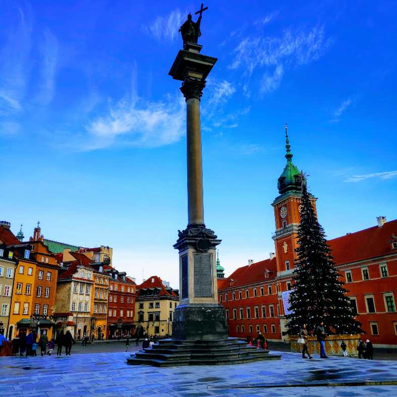 a statue in the warsaw old town with the warsaw castle in the background