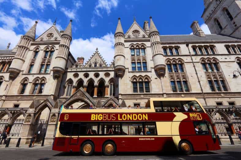 A double decker hop on hop off bus in London parked outside a historic building
