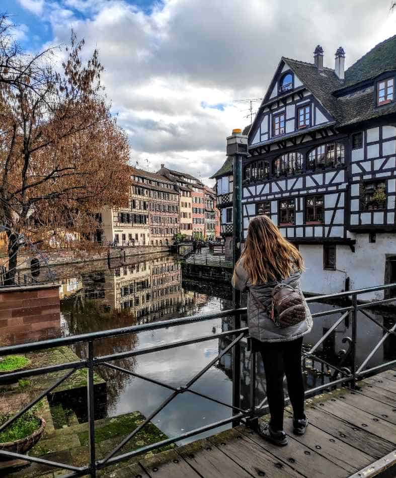 A blonde teen looking out over the cananl towards the wooden thatched houses in Strasbourg France.