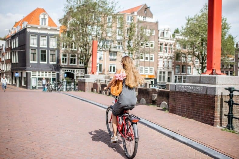 a teenage girl riding her bike in Amsterdam over a canal bridge