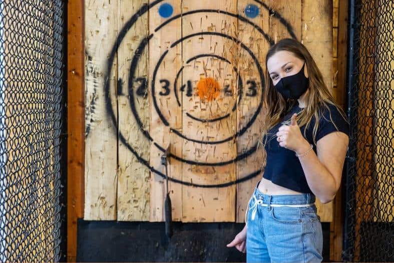a teenagers girl doing axe throwing, standing infront of the target area