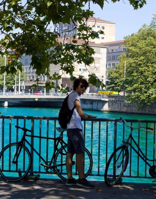 standing by the water in Zurich is a teenager with his bike
