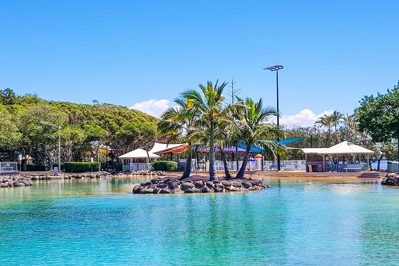 a peaceful, man-made lagoon surrounded by sandy shores and palm trees at the Redcliffe Settlement Lagoon in Brisbane
