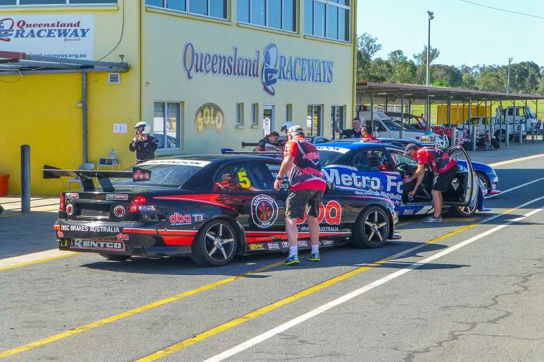 a high-speed V8 racecar in action, surrounded by the intense atmosphere of the race track at the Queensland Raceway in Brisbane