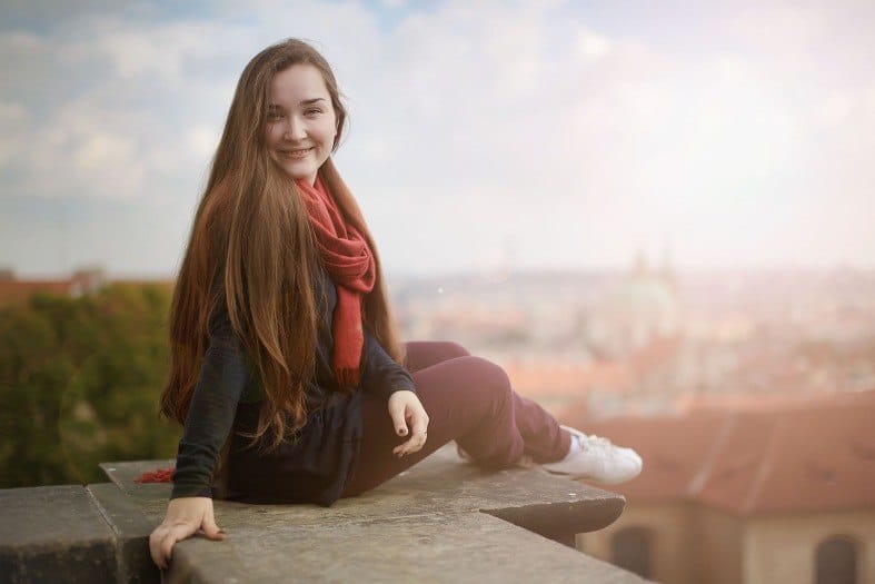 a teenager in Prague at a lookout looking straight at the camera and giving a big smile. the city in the background is blurred but you can make out a few buildings. The best things to do in Prague