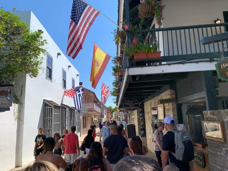 St Augustine with teenagers is great to experience. Here is a busy street filled with people walking. The high buildings provide shade to the pedestrians and there are flags flying from the second story of the old-style shops.