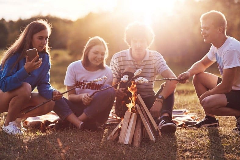 Teenagers sitting around a camp fore toasting marshmellows
