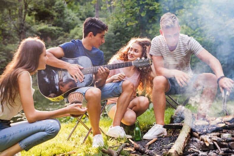 Teens sitting around a fire playing guitar