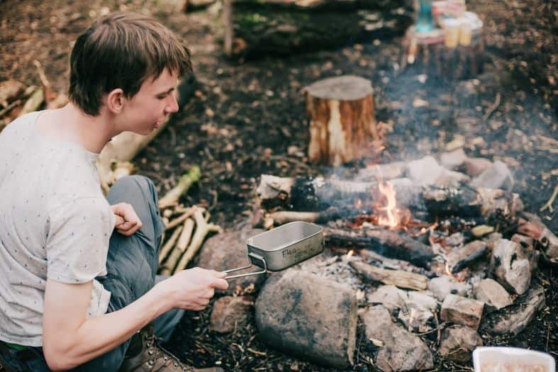 A teenager cooking some food over the campfire