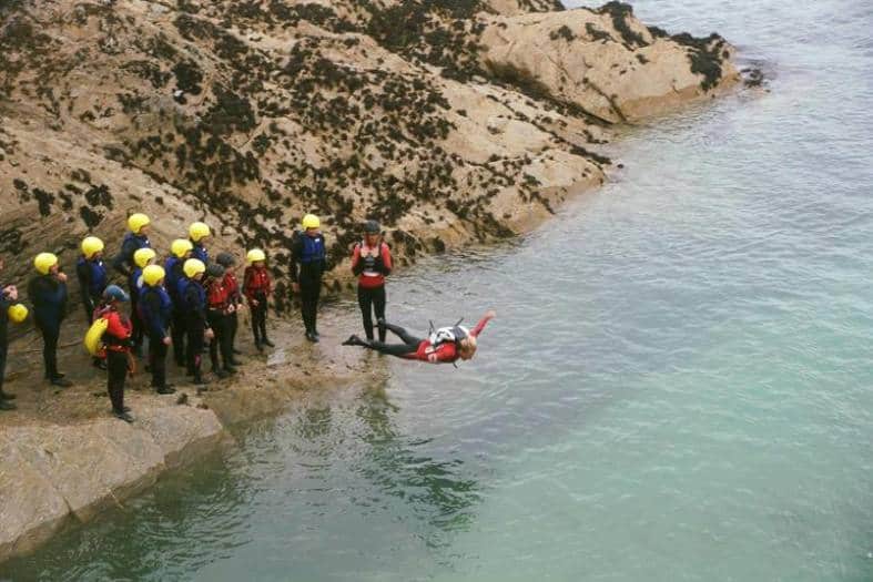 individuals navigating rocky cliffs and dynamic coastal terrain at the thrilling coasteering adventure in England