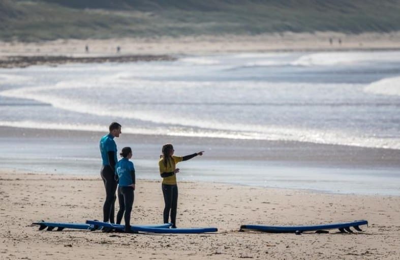 an instructor on a beach in Scotland teaching teenagers how to surf