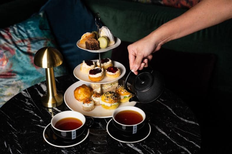 A beautifully arranged table with dainty teacups, saucers, and tiered trays displaying an assortment of delectable pastries, sandwiches, and treats of a high tea experience in Brisbane, Queensland