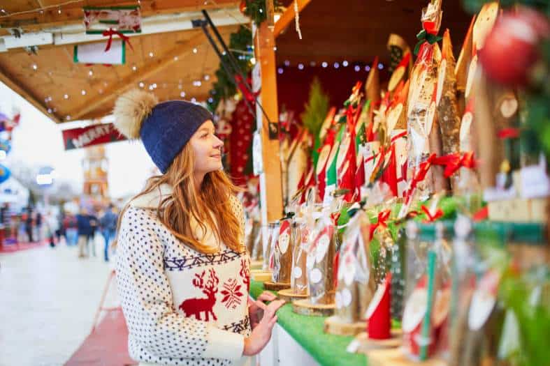 A young female adult looking at colourful ornaments displayed in a wooden stall at one of the best European Christmas Markets for teenagers