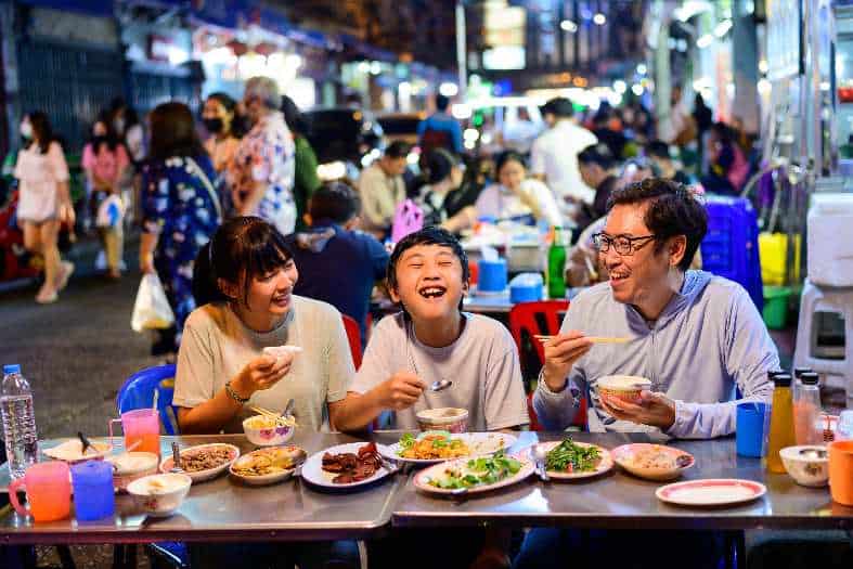 A family sitting in Bangkok trying different types of street food
