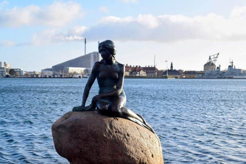 Iconic Little Mermaid statue in Copenhagen against a scenic backdrop, symbolizing the enchanting charm of the city